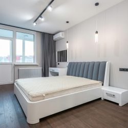 Spacious minimalist bedroom featuring modern design elements with white walls and parquet flooring.